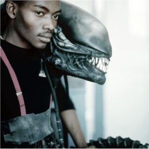 Image of Bolaji Badejo with Alien costume in the background